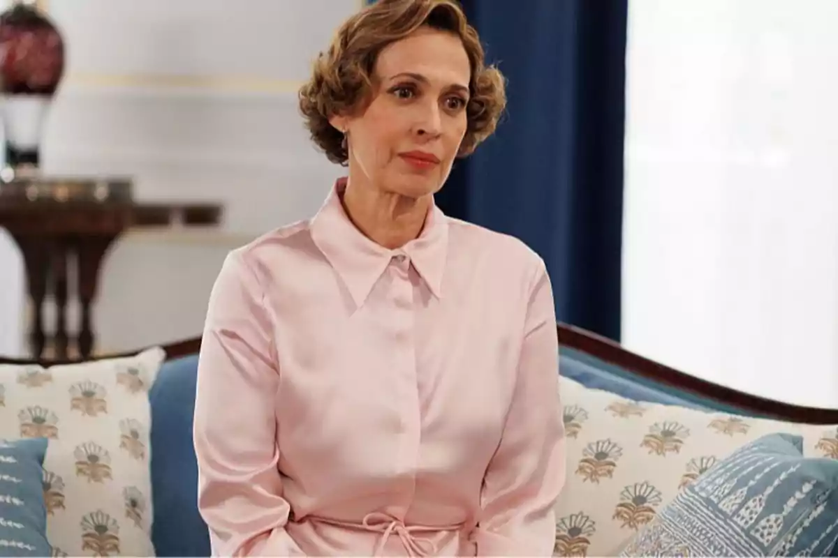 Maruja con cabello corto y ondulado sentada en un sofá con cojines decorativos y vistiendo una blusa rosa claro. Captura de 'La Moderna'