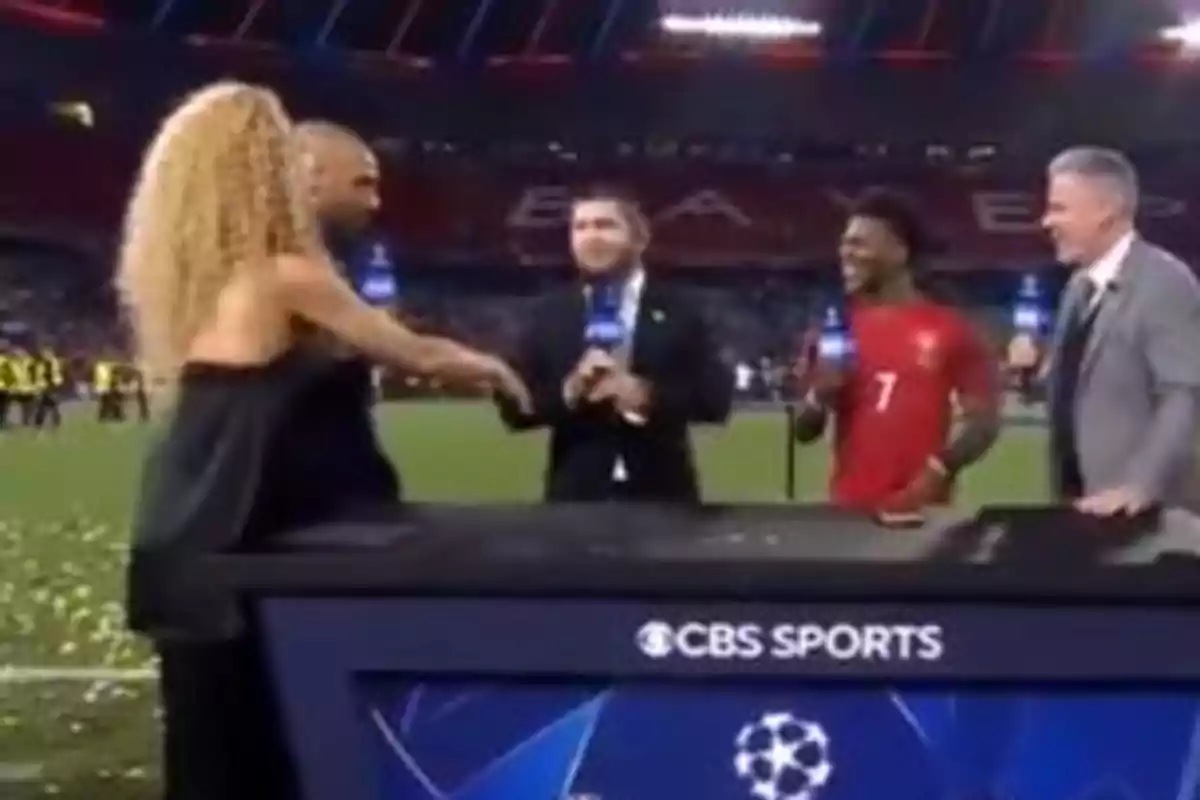 Cuatro personas conversan y sonríen en un set de transmisión deportiva en un estadio de fútbol, con el logo de CBS Sports visible en la mesa. Cuatro personas conversan y sonríen en un set de transmisión deportiva en un estadio de fútbol, con el logo de CBS Sports visible en la mesa.