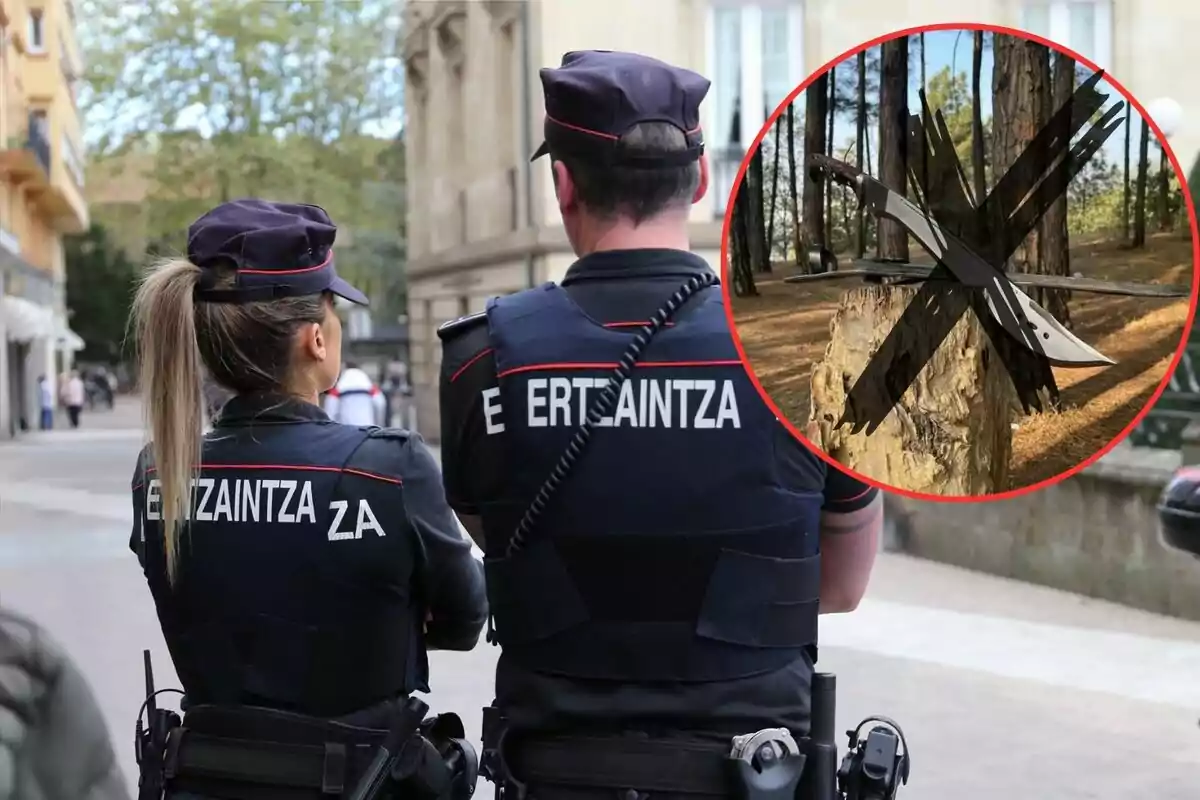 Dos agentes de la Ertzaintza de espaldas, con un círculo rojo que muestra un árbol con cuchillos clavados y una cruz negra sobre ellos.