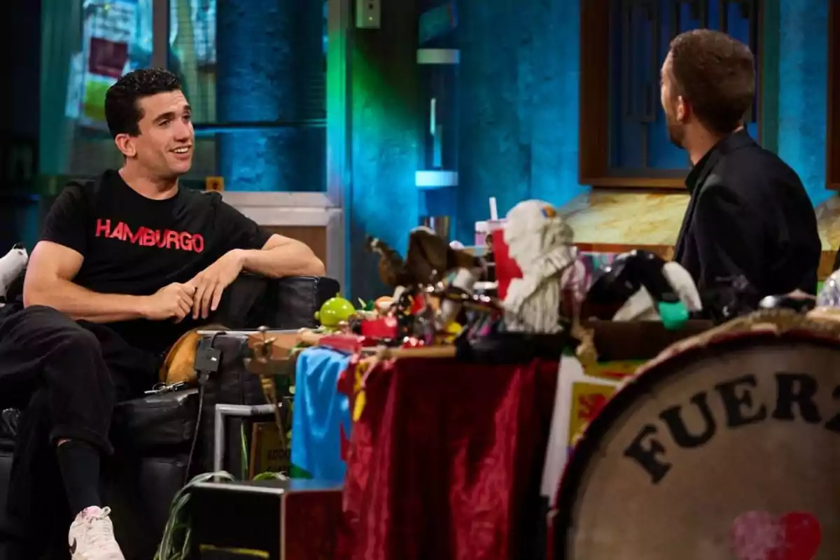 Jaime Lorente y David Broncano conversan en un set de televisión decorado con objetos variados y coloridos. Captura de 'La Revuelta' Jaime Lorente y David Broncano conversan en un set de televisión decorado con objetos variados y coloridos. Captura de 'La Revuelta'