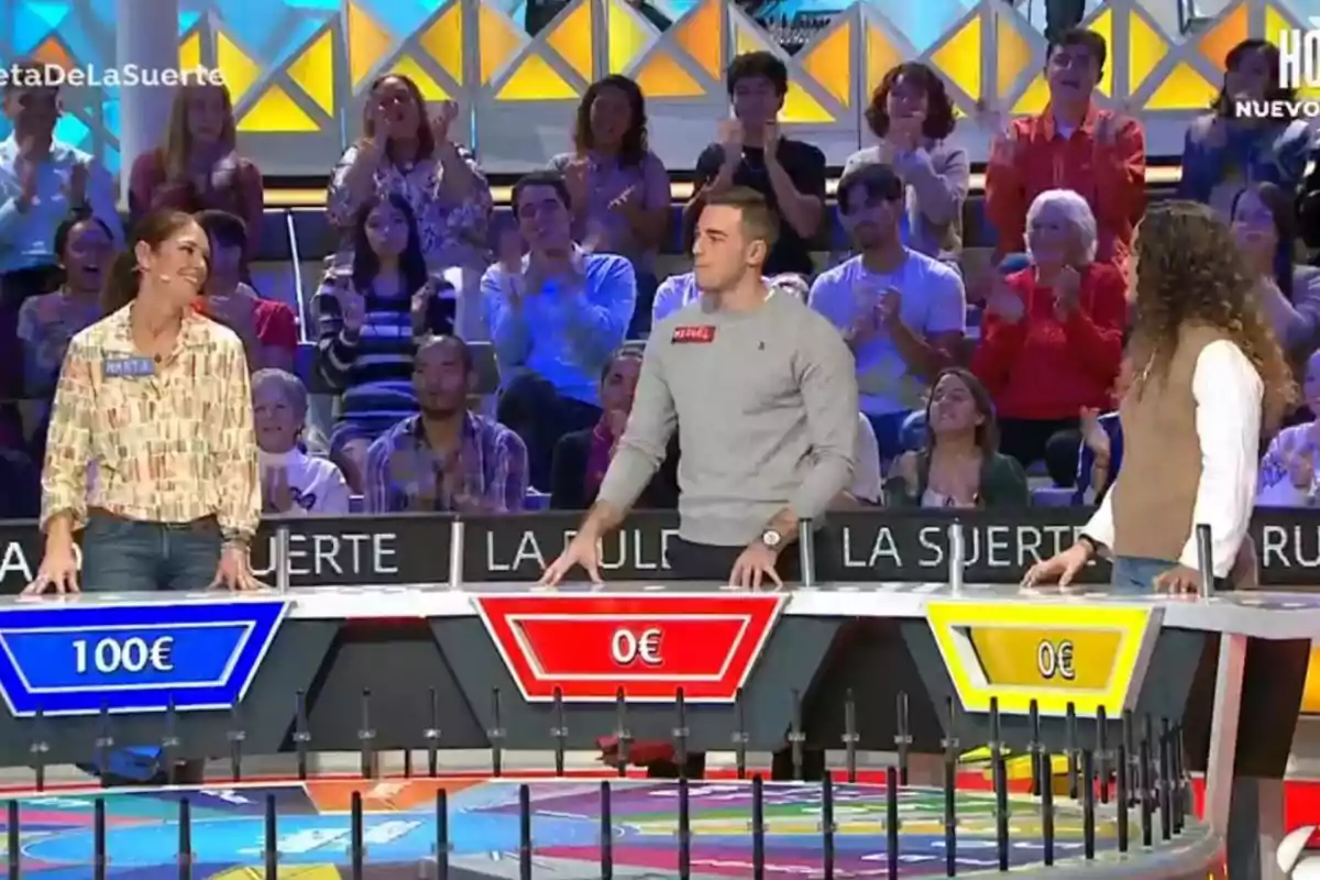 Three contestants take part in a television game show, with an audience applauding in the background. Still from 'La Ruleta de la Suerte'