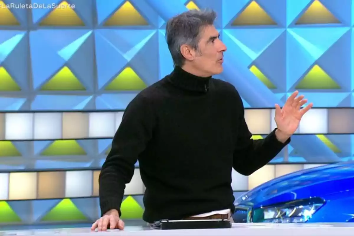 Jorge Fernández de pie con un suéter negro gesticula mientras está frente a un fondo geométrico colorido. Captura de 'La Ruleta de la Suerte' Jorge Fernández de pie con un suéter negro gesticula mientras está frente a un fondo geométrico colorido. Captura de 'La Ruleta de la Suerte'