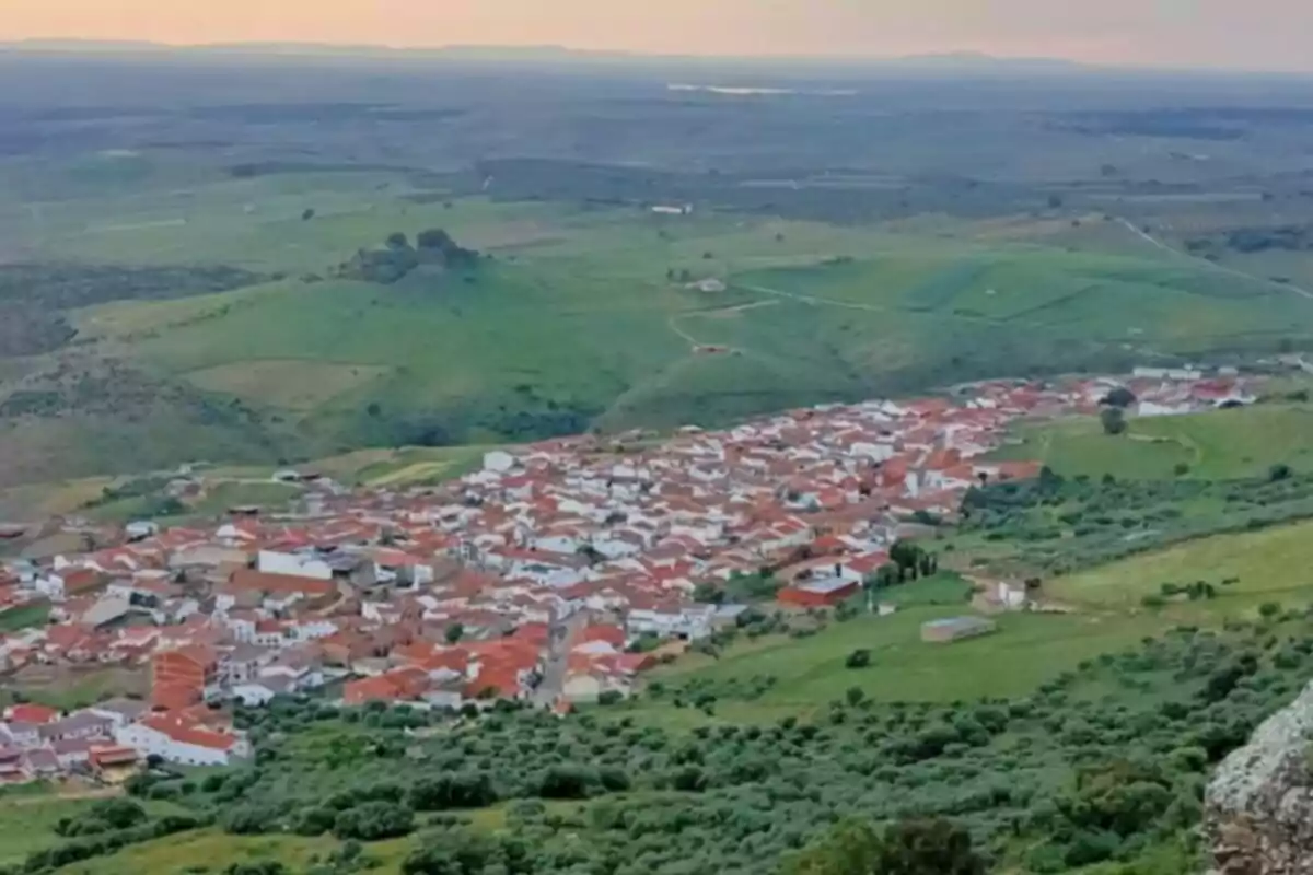 Vista panorámica de un pueblo rodeado de colinas verdes y campos al atardecer.