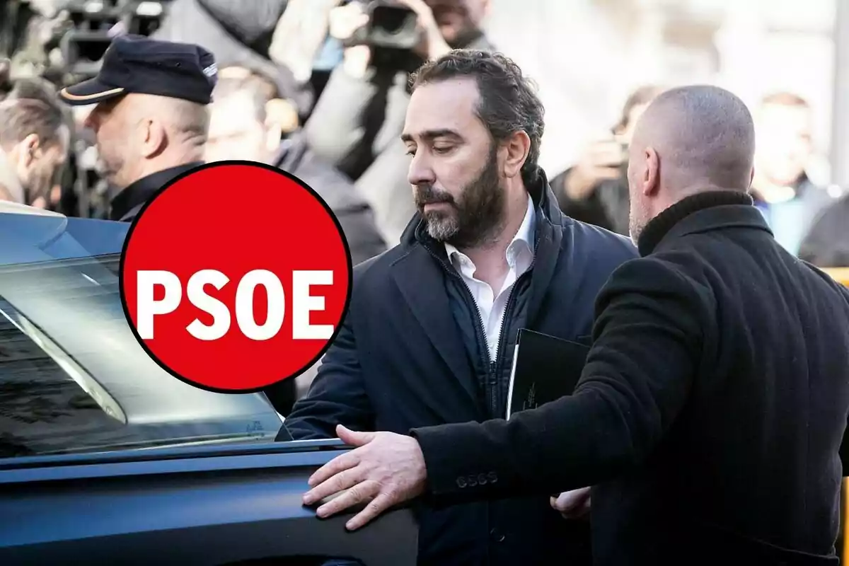 Un hombre con barba y chaqueta oscura es escoltado hacia un automóvil mientras un grupo de personas lo rodea; en la imagen aparece un logotipo rojo con las letras "PSOE".