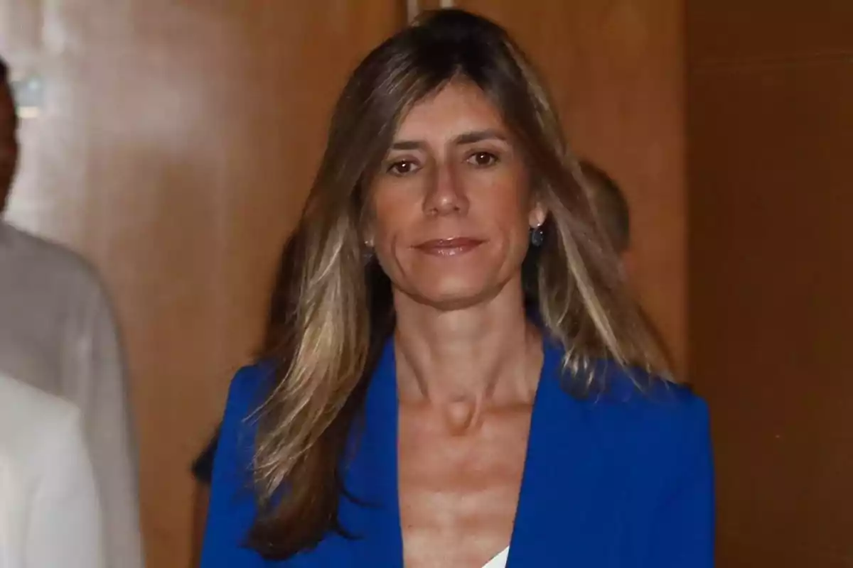 Mujer con cabello largo y rubio, vistiendo un blazer azul, en un entorno interior.