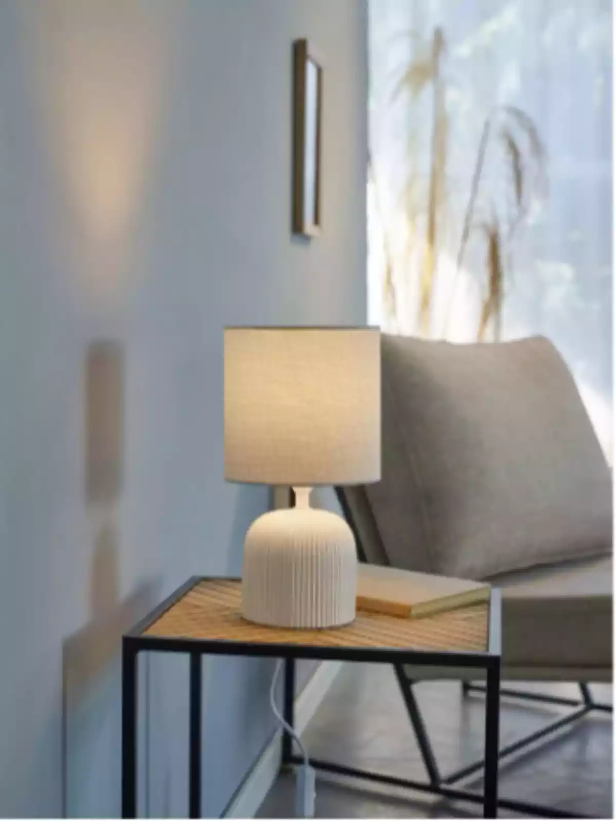 Lámpara de mesa encendida sobre una mesa auxiliar junto a un sillón en una sala iluminada por luz natural Lámpara de mesa encendida sobre una mesa auxiliar junto a un sillón en una sala iluminada por luz natural