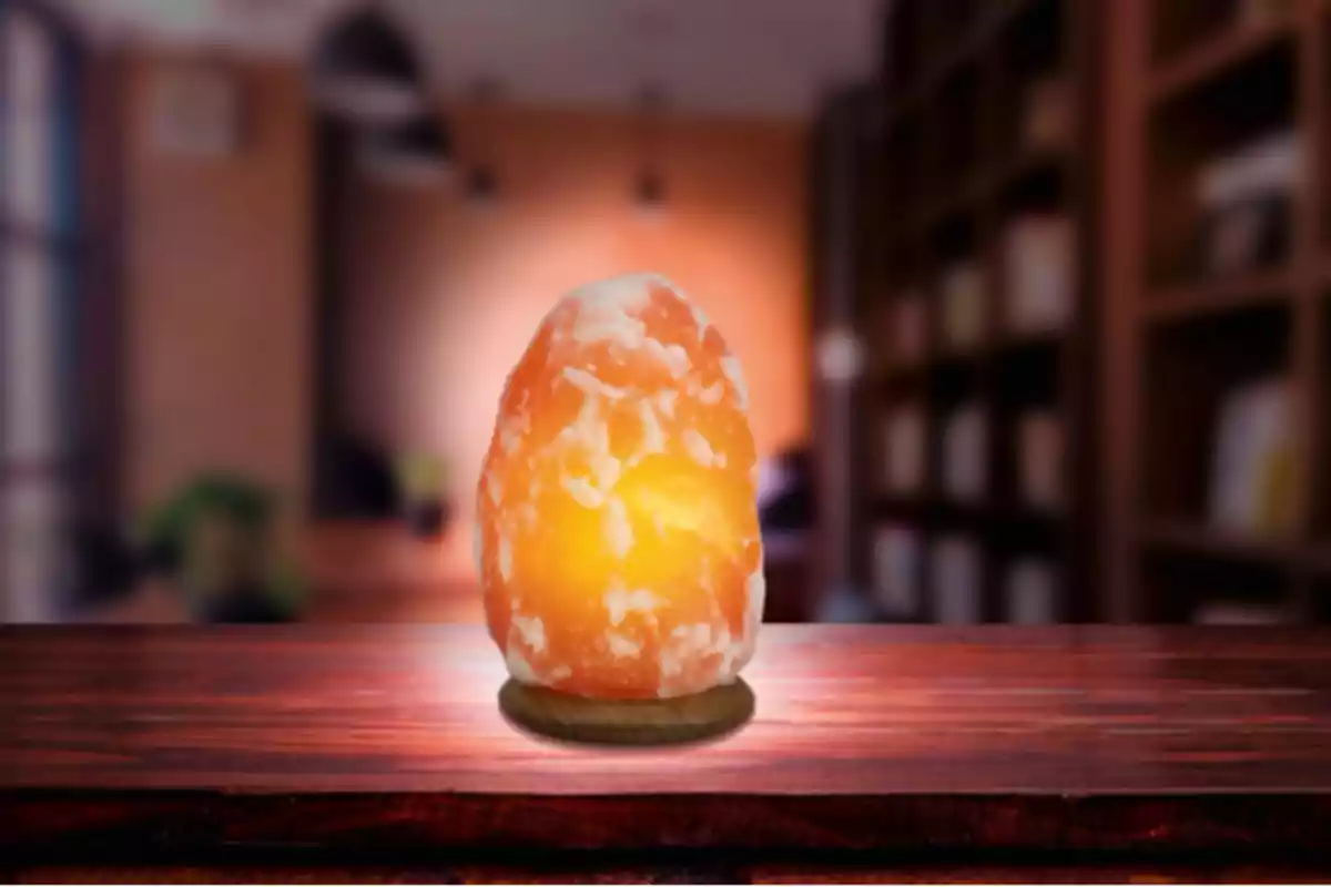 Lámpara de sal encendida sobre una mesa de madera con un fondo desenfocado de estanterías y luces cálidas Lámpara de sal encendida sobre una mesa de madera con un fondo desenfocado de estanterías y luces cálidas