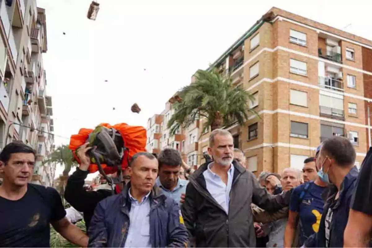 Un grupo de personas camina por una calle rodeada de edificios mientras algunos objetos vuelan en el aire.