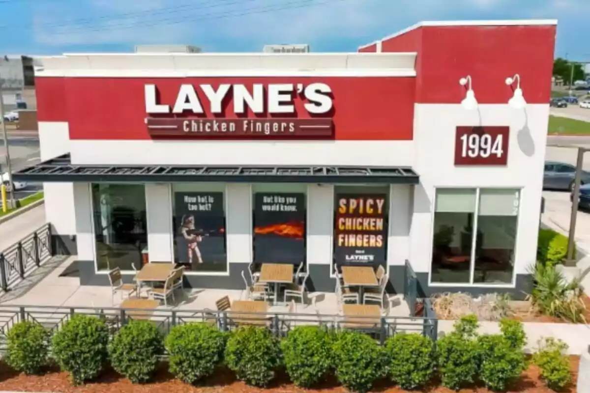 Frente de un restaurante Layne's Chicken Fingers con mesas al aire libre y carteles promocionales en las ventanas. Frente de un restaurante Layne's Chicken Fingers con mesas al aire libre y carteles promocionales en las ventanas.