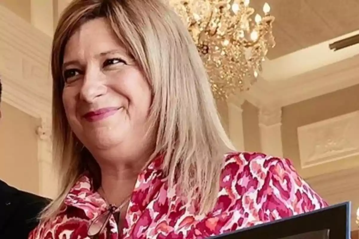 Mujer de cabello rubio sonriente con blusa de estampado rojo y fondo elegante con lámpara de araña. Mujer de cabello rubio sonriente con blusa de estampado rojo y fondo elegante con lámpara de araña.