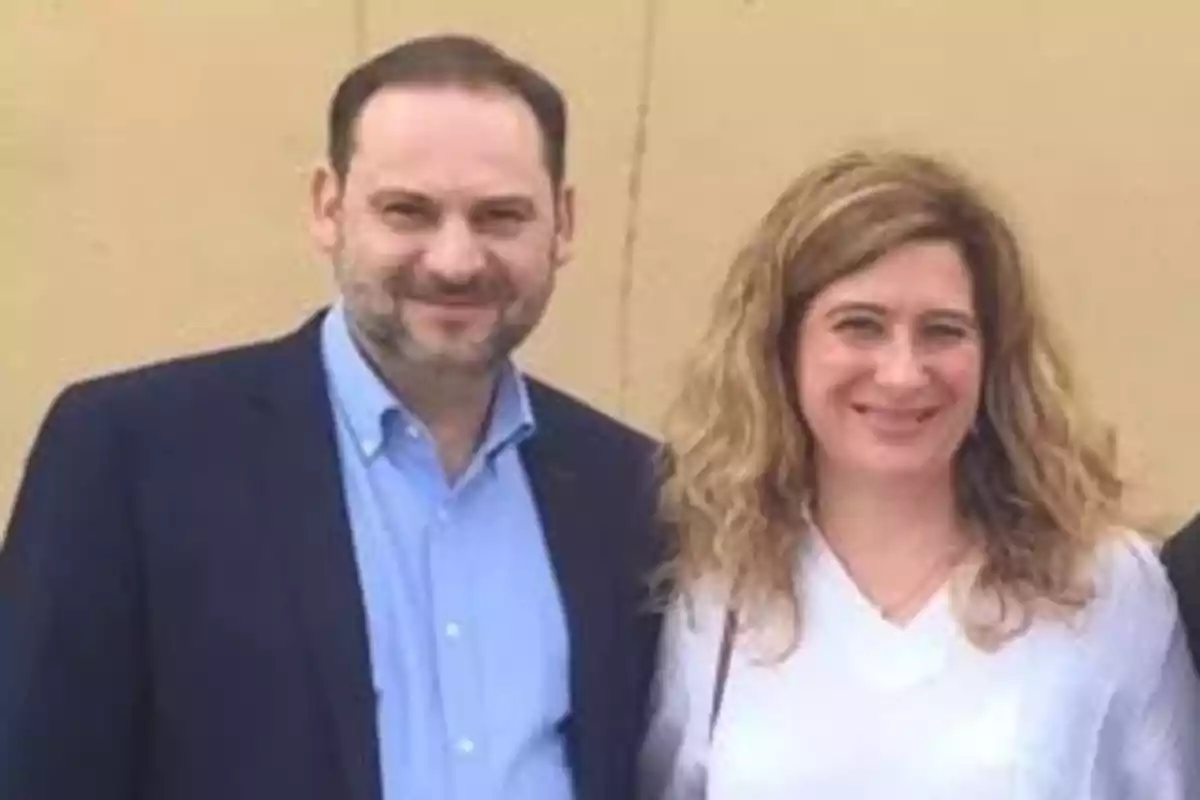 Un hombre con barba y una mujer de cabello rubio y ondulado posan juntos sonriendo frente a una pared beige. Un hombre con barba y una mujer de cabello rubio y ondulado posan juntos sonriendo frente a una pared beige.