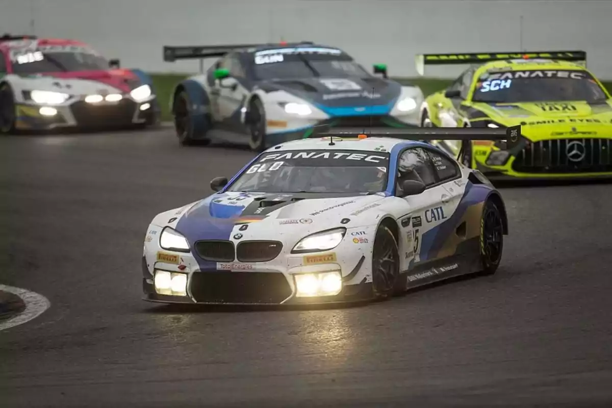 Cuatro autos de carreras compiten en una pista, con un BMW blanco y azul en primer plano liderando la carrera.