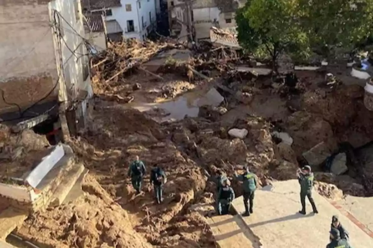 Personas caminando por una zona afectada por un deslizamiento de tierra en un área urbana con escombros y barro.