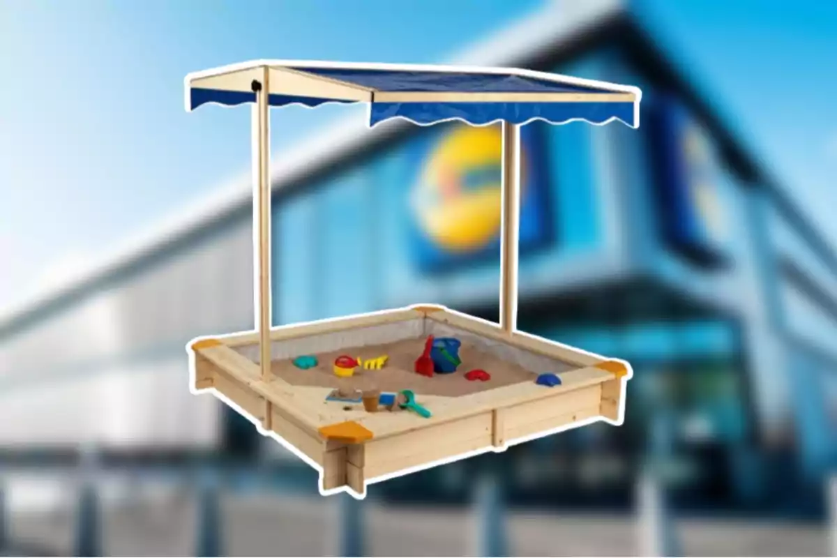 Arenero de madera con toldo azul y juguetes infantiles sobre un fondo borroso de supermercado Arenero de madera con toldo azul y juguetes infantiles sobre un fondo borroso de supermercado