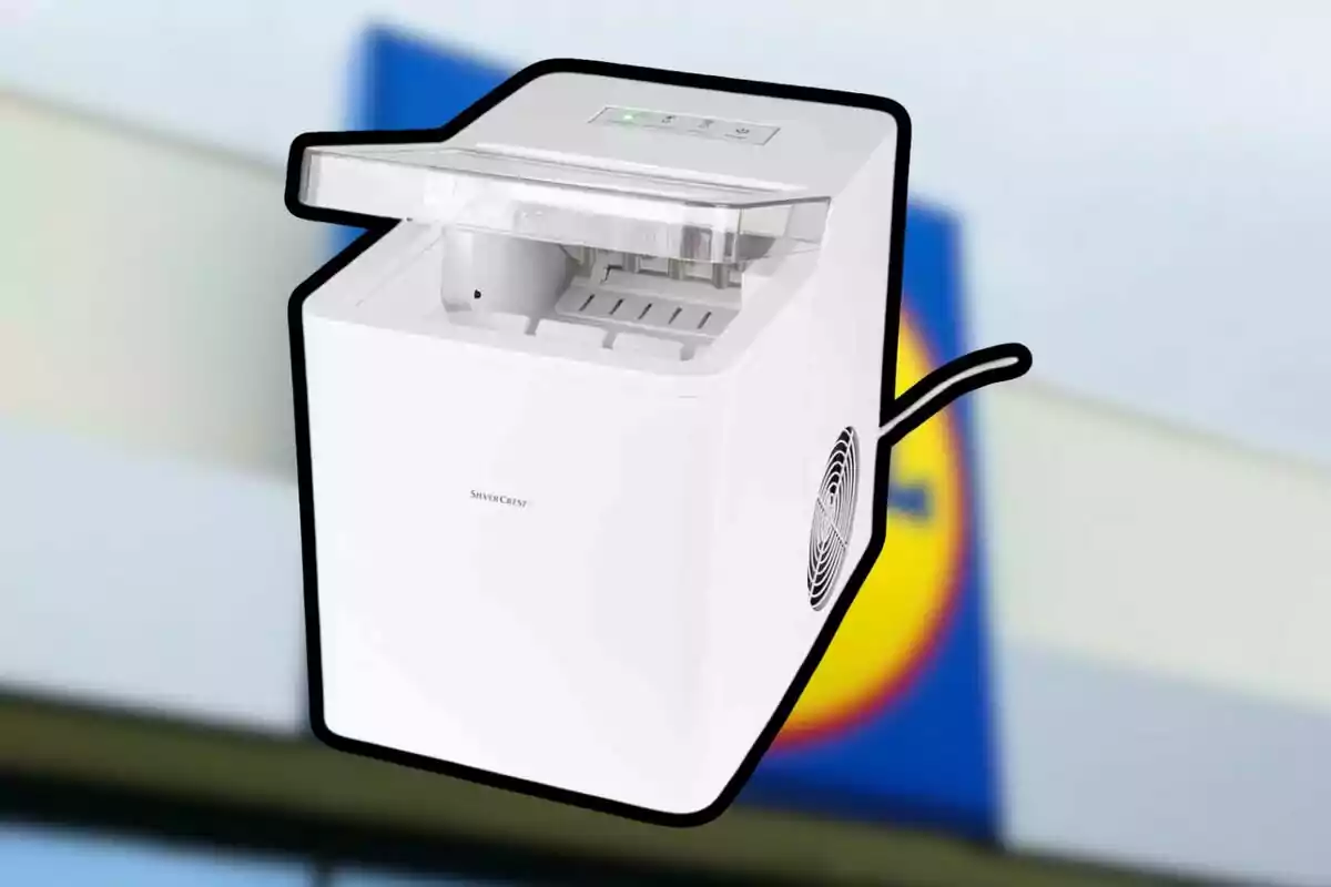 Máquina de hacer hielo de color blanco con tapa transparente y controles en la parte superior, con un fondo desenfocado que parece ser un cartel de supermercado. Máquina de hacer hielo de color blanco con tapa transparente y controles en la parte superior, con un fondo desenfocado que parece ser un cartel de supermercado.