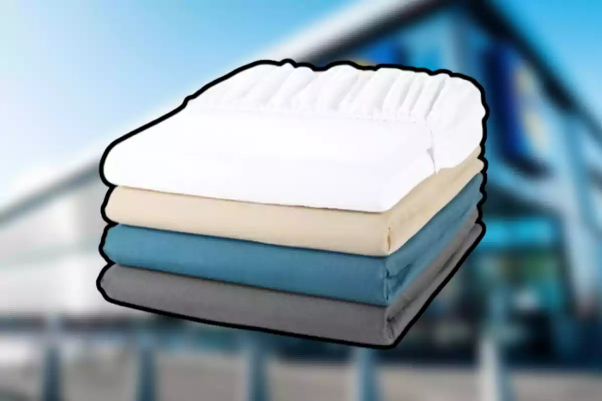 Cuatro sábanas de diferentes colores dobladas y apiladas frente a un fondo desenfocado de un edificio. Cuatro sábanas de diferentes colores dobladas y apiladas frente a un fondo desenfocado de un edificio.