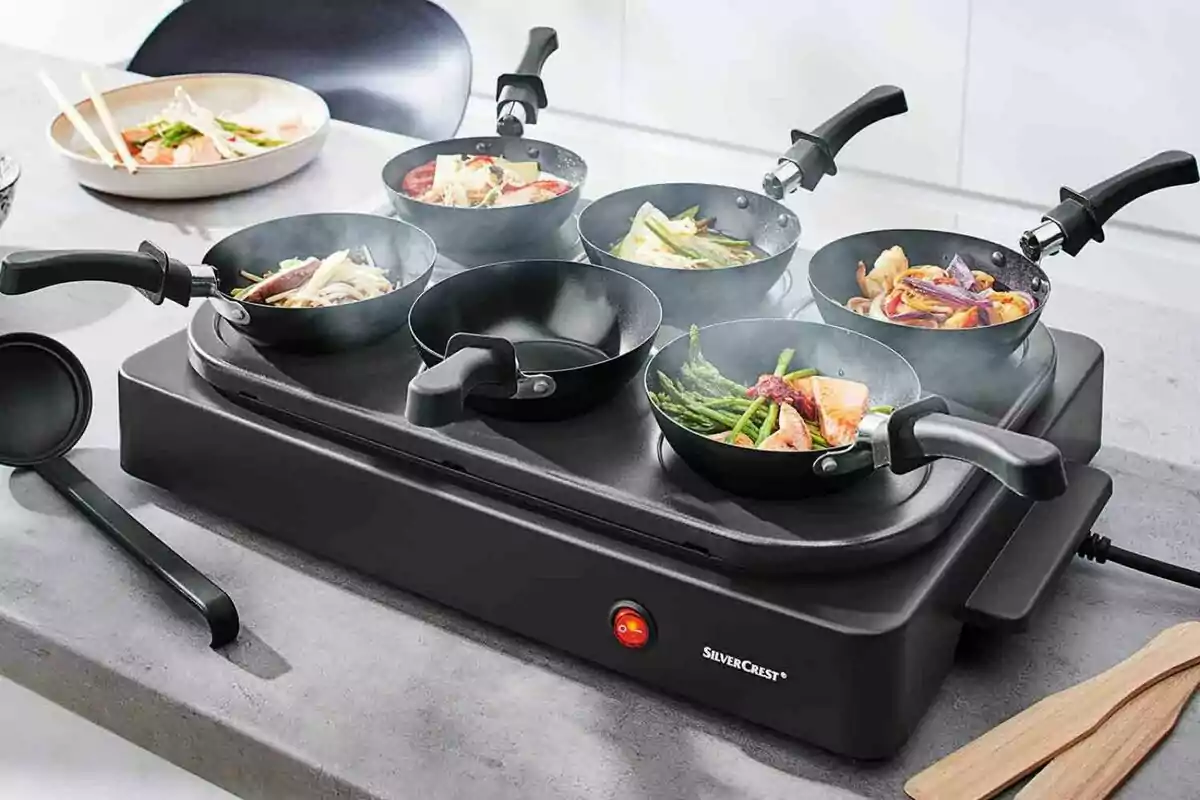 Una parrilla eléctrica con varias sartenes pequeñas cocinando diferentes tipos de alimentos. Una parrilla eléctrica con varias sartenes pequeñas cocinando diferentes tipos de alimentos.