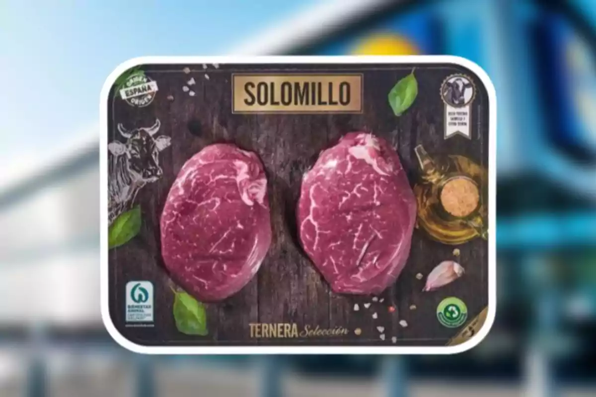 La imagen muestra un paquete de solomillo de ternera con dos piezas de carne cruda en un fondo oscuro decorado con hojas verdes, un dibujo de vaca, un recipiente de aceite, sal y un diente de ajo. La imagen muestra un paquete de solomillo de ternera con dos piezas de carne cruda en un fondo oscuro decorado con hojas verdes, un dibujo de vaca, un recipiente de aceite, sal y un diente de ajo.