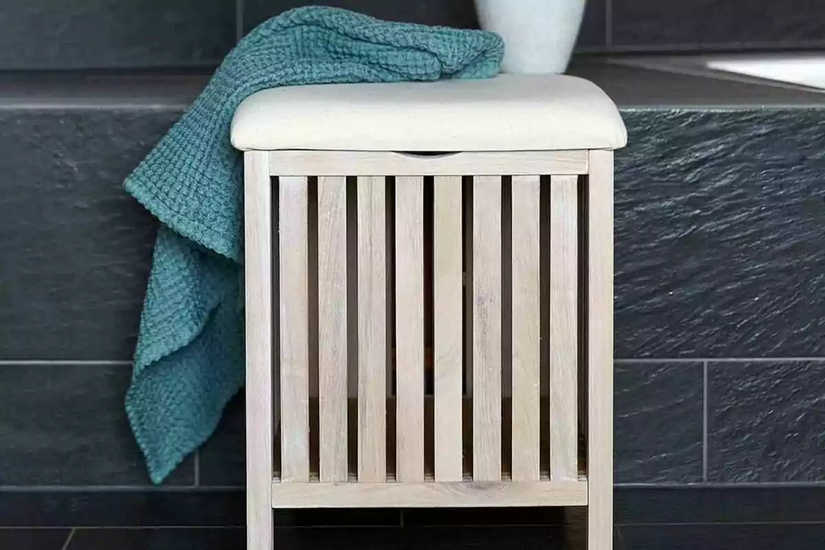 Banco de madera con cojín blanco y manta azul en un baño con azulejos oscuros. Banco de madera con cojín blanco y manta azul en un baño con azulejos oscuros.