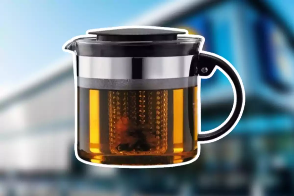 Tetera de vidrio con infusor de metal y tapa negra, contiene una bebida color ámbar y está sobre un fondo desenfocado. Tetera de vidrio con infusor de metal y tapa negra, contiene una bebida color ámbar y está sobre un fondo desenfocado.