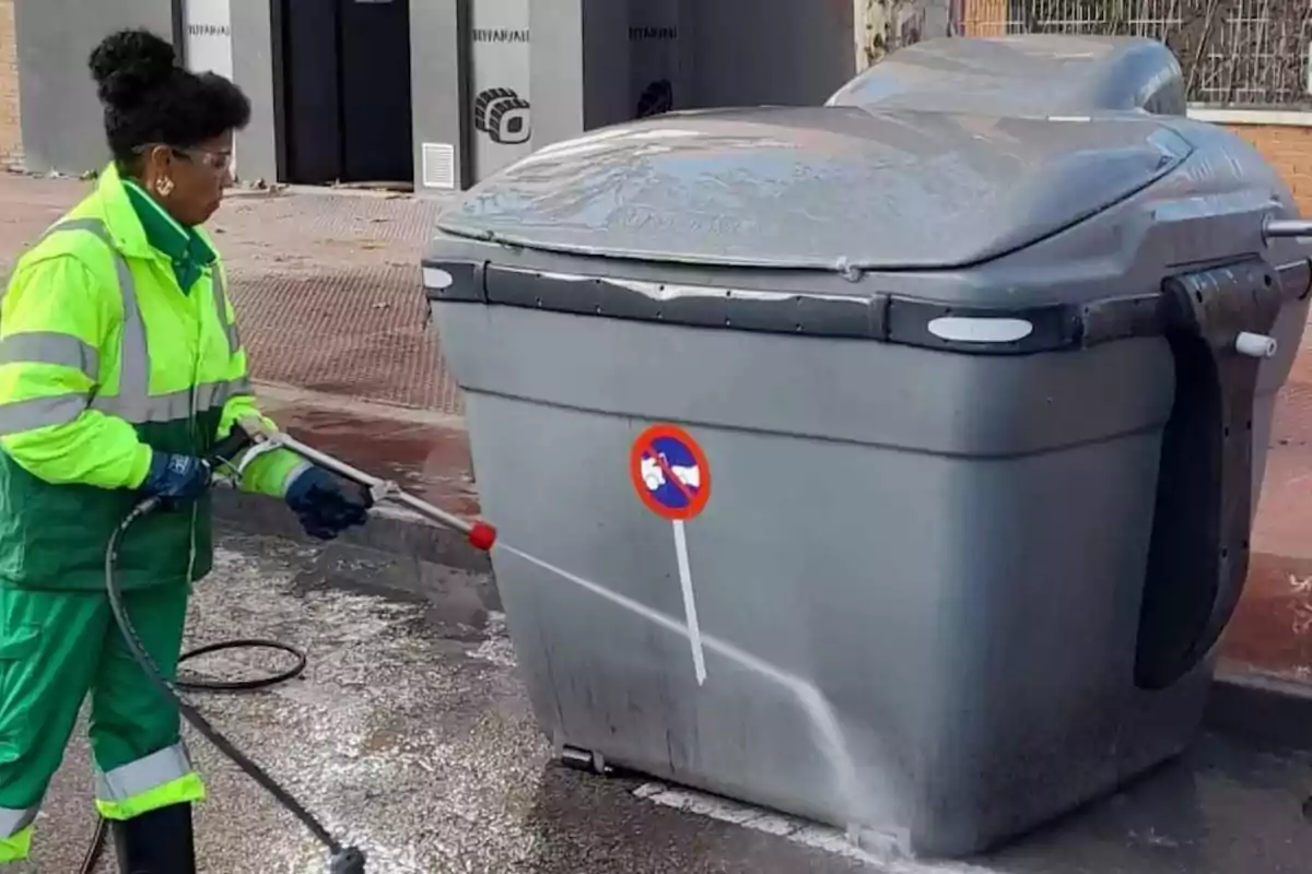 Una mujer lava un contenedor en la calle con una manguera de agua a presión