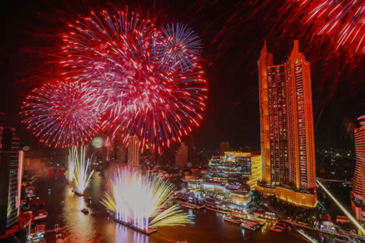 Fuegos artificiales iluminan el cielo nocturno sobre una ciudad con rascacielos y un río.