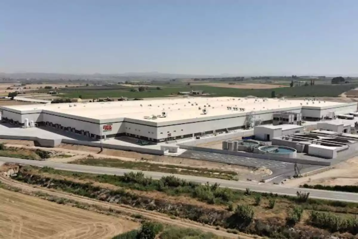 Vista aérea de un gran edificio industrial rodeado de campos y caminos en un paisaje rural.