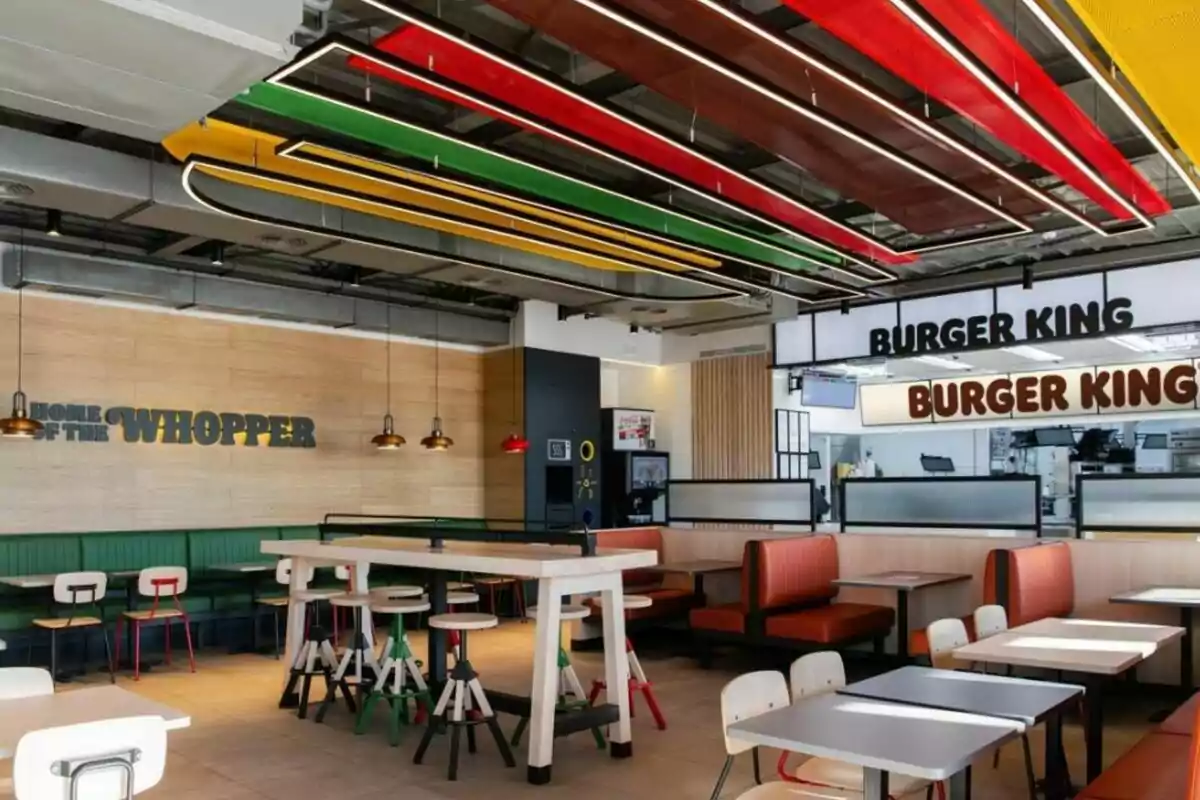 Interior de un restaurante de Burger King con mesas, sillas y decoración colorida en el techo. Interior de un restaurante de Burger King con mesas, sillas y decoración colorida en el techo.