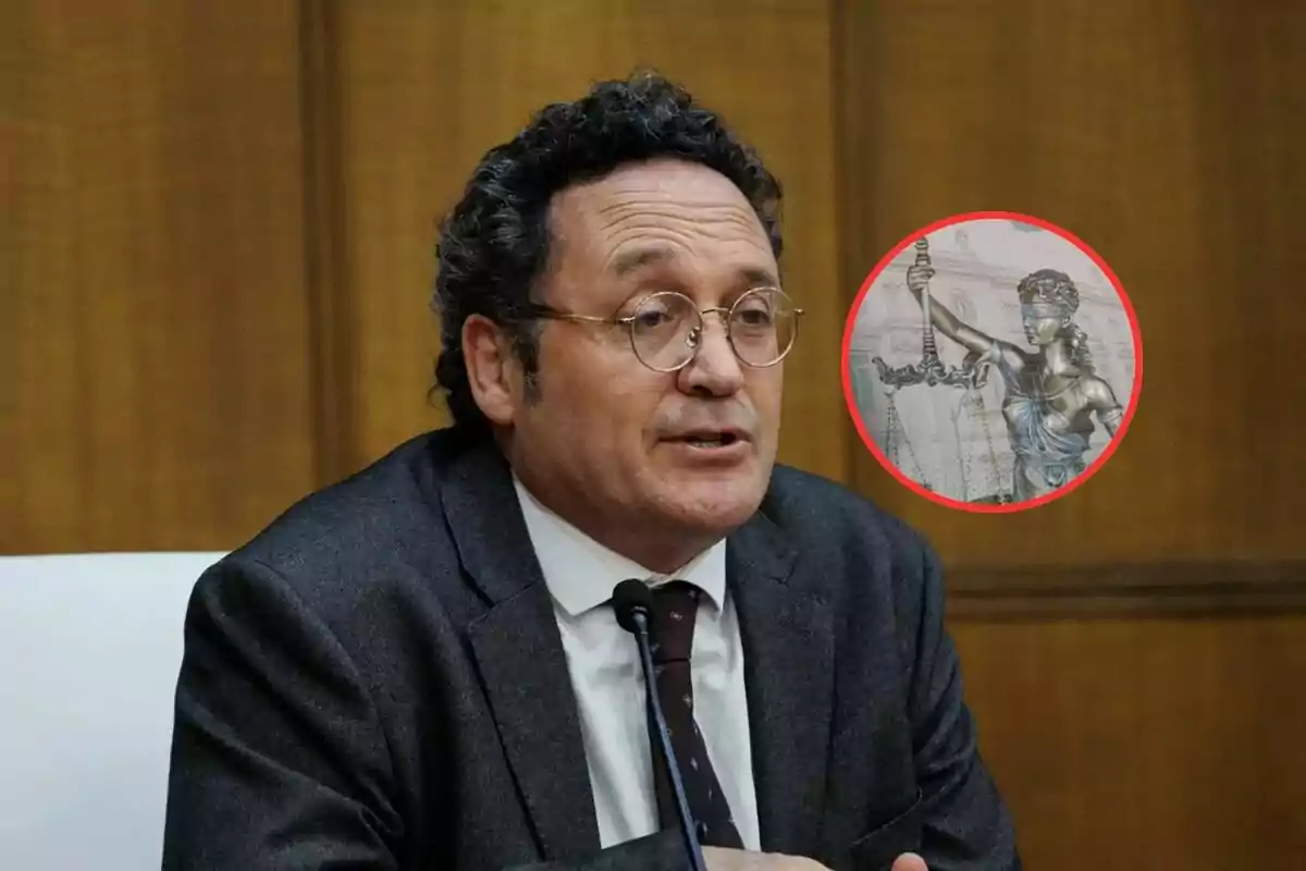 Hombre de cabello rizado y gafas hablando frente a un micrófono con fondo de madera y un círculo que muestra la imagen de una estatua de la justicia