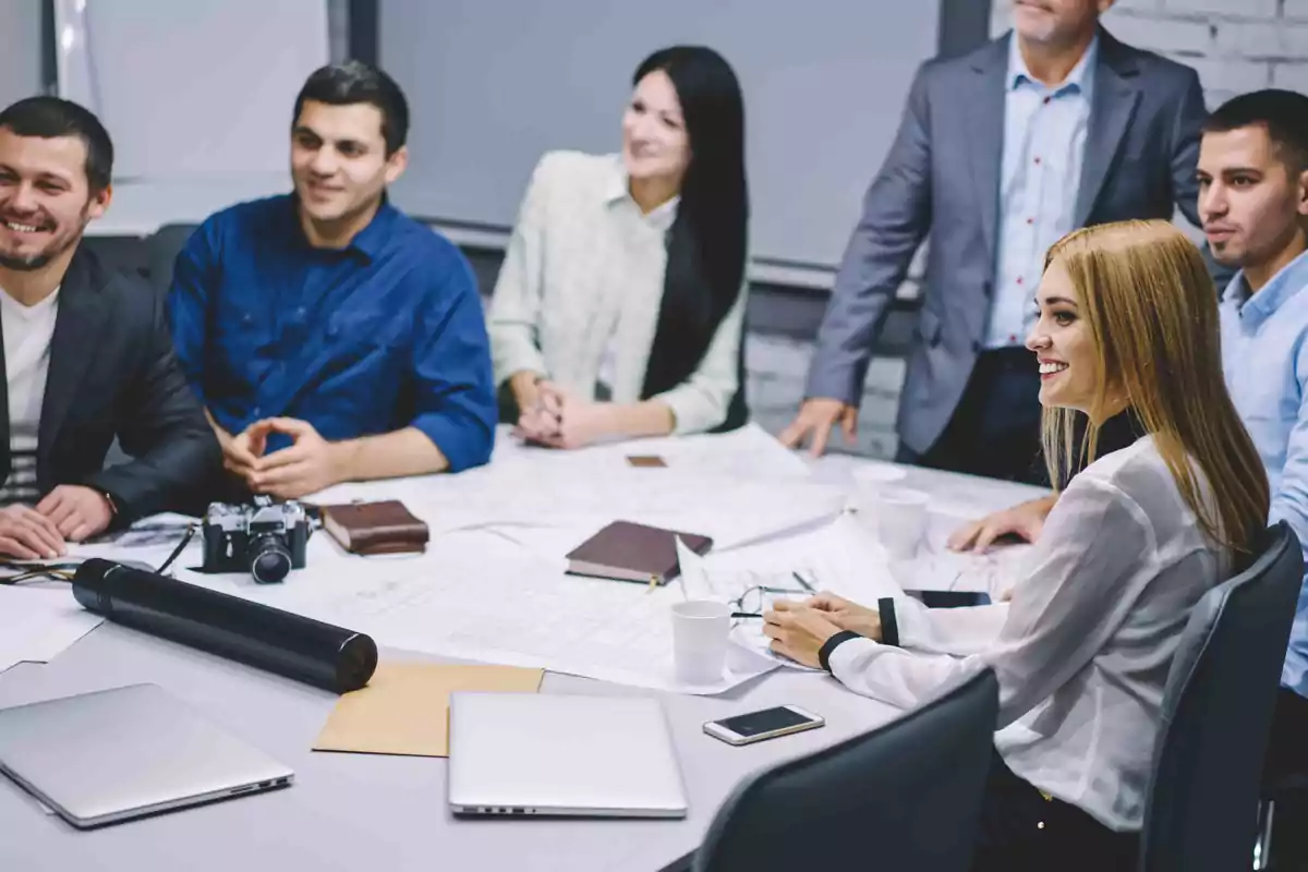 Grupo de personas en una reunión de trabajo alrededor de una mesa con documentos y dispositivos electrónicos.