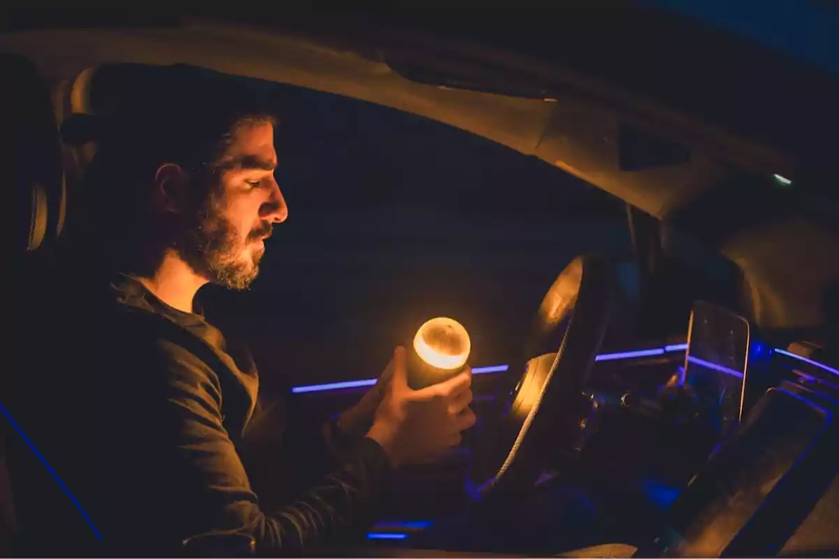 Hombre dentro de un auto sosteniendo una luz cálida en la mano mientras mira hacia abajo.