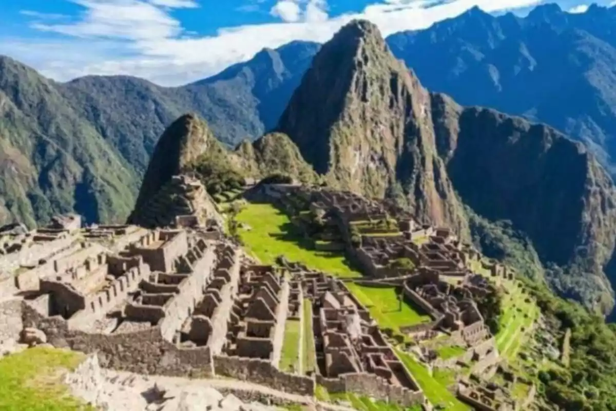 Vista panorámica de las ruinas de Machu Picchu con montañas al fondo bajo un cielo parcialmente nublado.