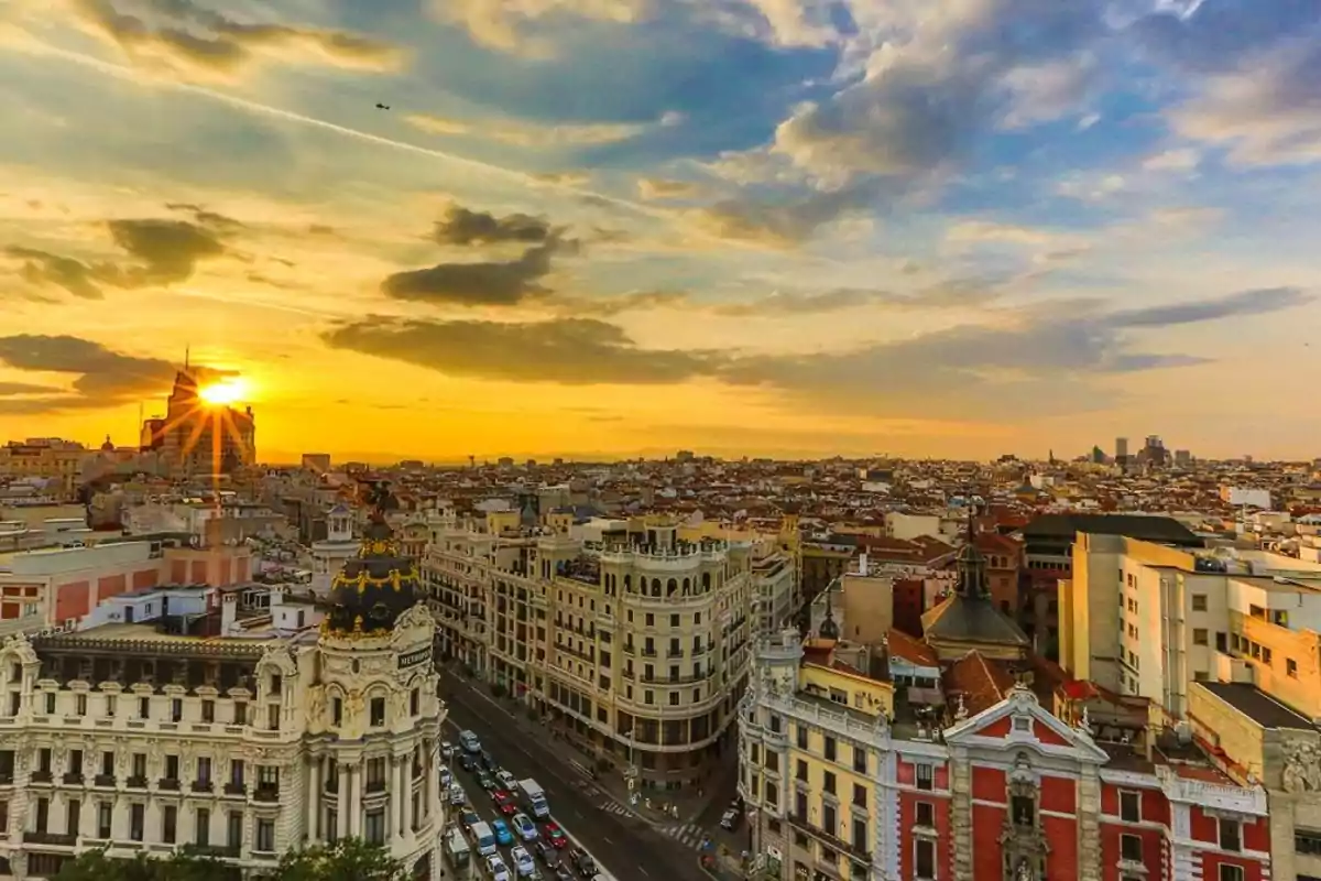 Vista panorámica de la ciudad de Madrid al atardecer con el sol ocultándose detrás de los edificios y un cielo parcialmente nublado