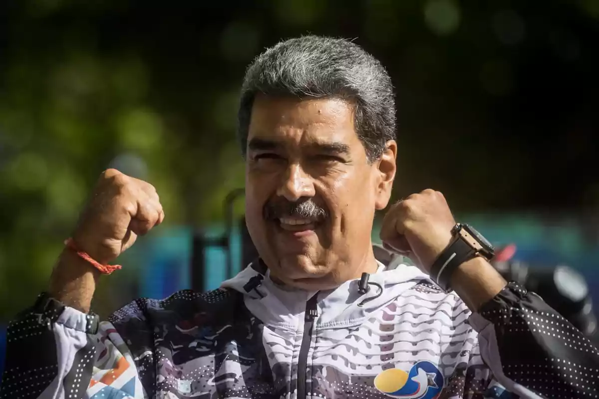 Un hombre con chaqueta deportiva levanta los puños en señal de victoria mientras sonríe.