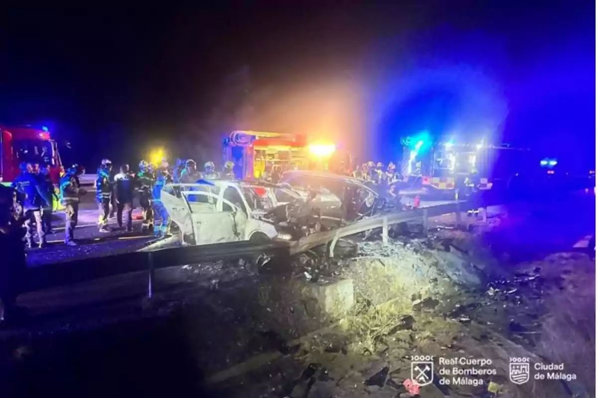Accidente de tráfico nocturno con varios bomberos y vehículos de emergencia atendiendo la escena donde dos coches han colisionado y uno de ellos está calcinado Accidente de tráfico nocturno con varios bomberos y vehículos de emergencia atendiendo la escena donde dos coches han colisionado y uno de ellos está calcinado