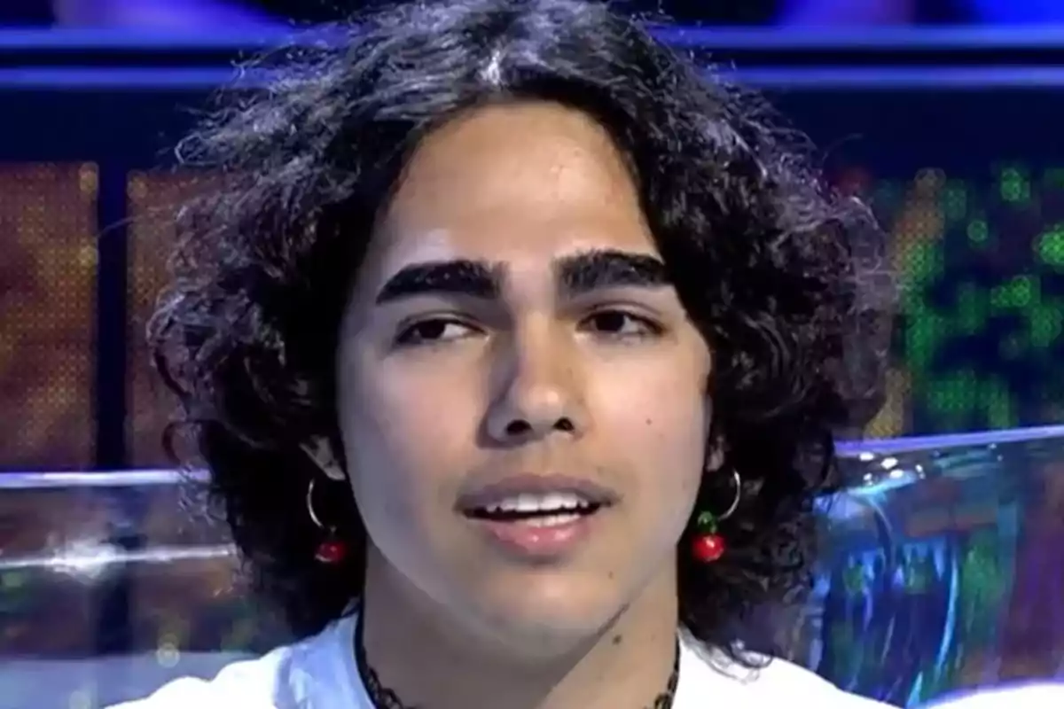 Manu Soto with curly hair and cherry earrings appears on a television show.