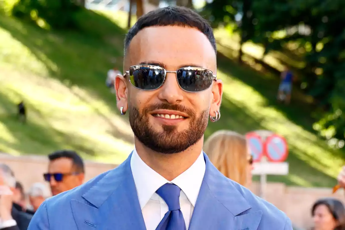 Manuel Cortés con gafas de sol vistiendo un traje azul y corbata, al aire libre en un evento social Manuel Cortés con gafas de sol vistiendo un traje azul y corbata, al aire libre en un evento social