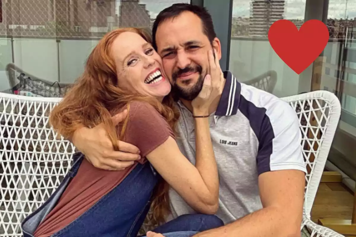 María Castro y José Manuel Villalba sonrientes abrazándose en una terraza con un corazón rojo en la esquina superior derecha.