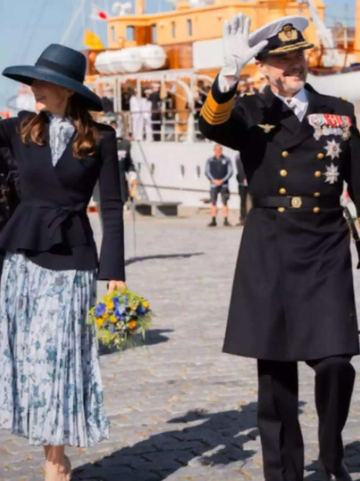 A woman in a floral dress and hat holds a bouquet of flowers while walking alongside a man in a naval uniform who is saluting, with a ship in the background. A woman in a floral dress and hat holds a bouquet of flowers while walking alongside a man in a naval uniform who is saluting, with a ship in the background.