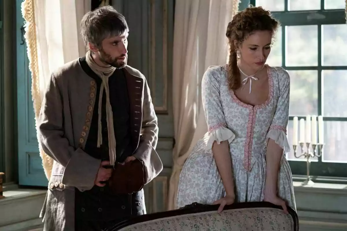 Chechu Salgado y Marina Sabadell, ambos con rostro serio, vestidos con ropa de época en una habitación iluminada por la luz natural que entra por una ventana. Chechu Salgado y Marina Sabadell, ambos con rostro serio, vestidos con ropa de época en una habitación iluminada por la luz natural que entra por una ventana.