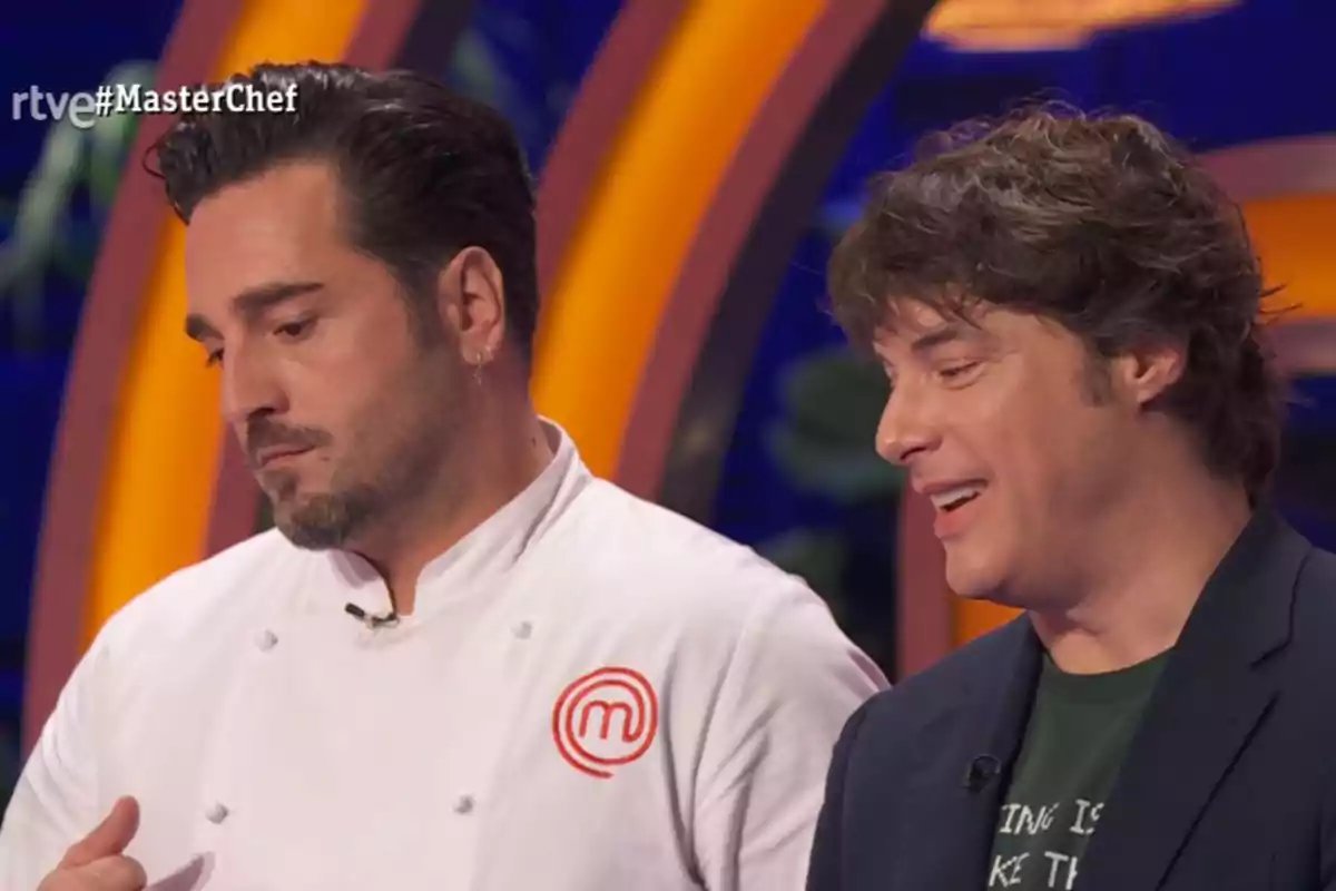 David Bustamante y Jordi Cruz conversan en un set de televisión de MasterChef uno de ellos lleva chaqueta de chef blanca y el otro viste camiseta y saco oscuro David Bustamante y Jordi Cruz conversan en un set de televisión de MasterChef uno de ellos lleva chaqueta de chef blanca y el otro viste camiseta y saco oscuro