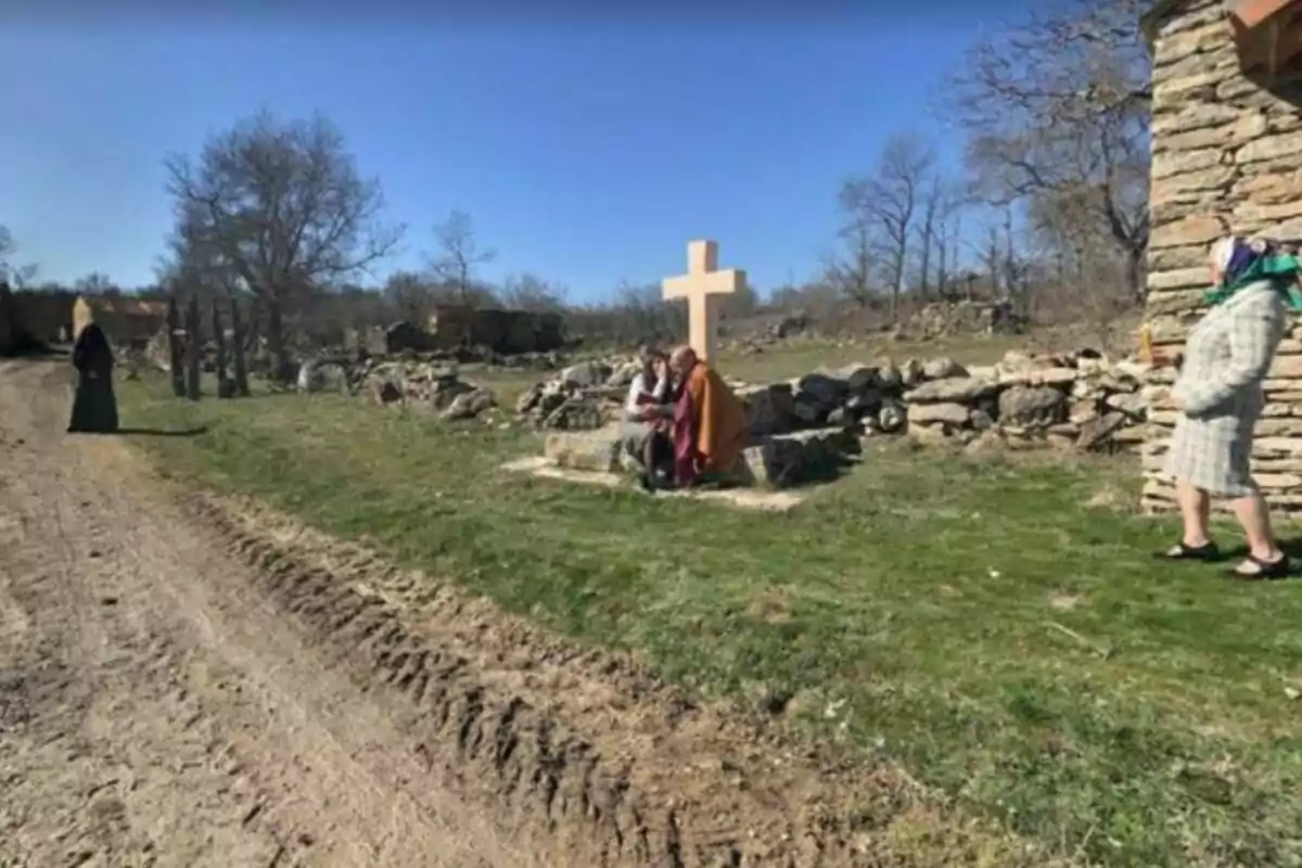 Personas vestidas con ropa tradicional en un entorno rural con una gran cruz de madera en el centro.