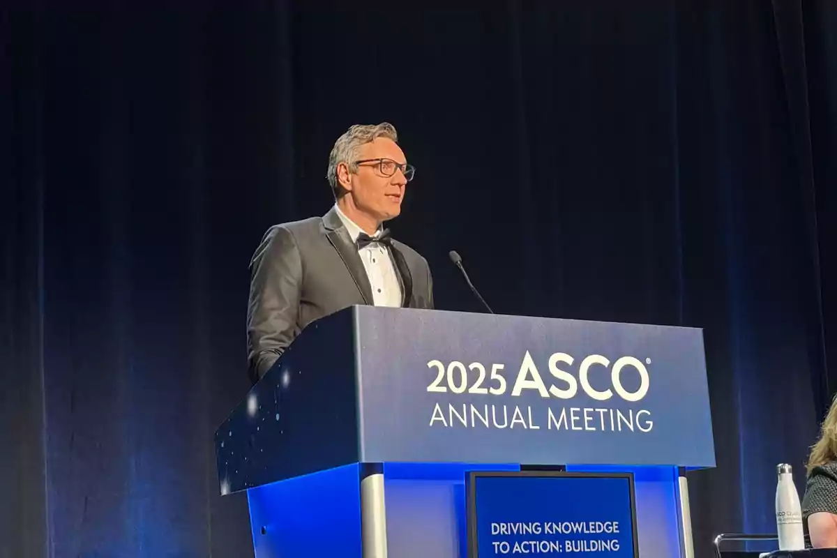 Un hombre con gafas y esmoquin habla en un podio durante la reunión anual de ASCO 2025