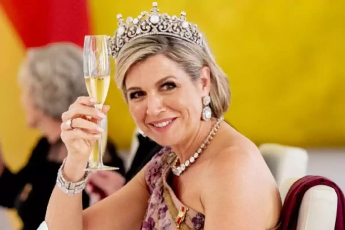 Mujer con tiara levantando una copa de champán y sonriendo en un evento formal.