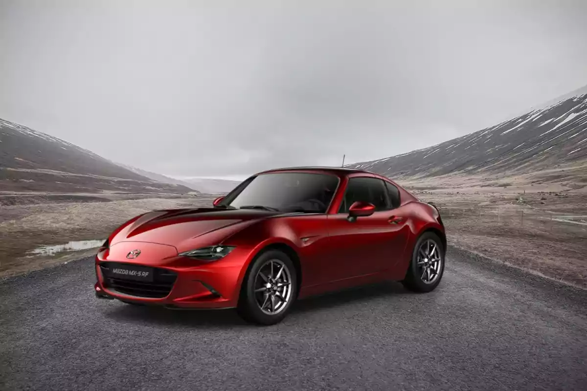 Un coche deportivo rojo Mazda MX-5 RF en una carretera con un paisaje montañoso y nublado de fondo.