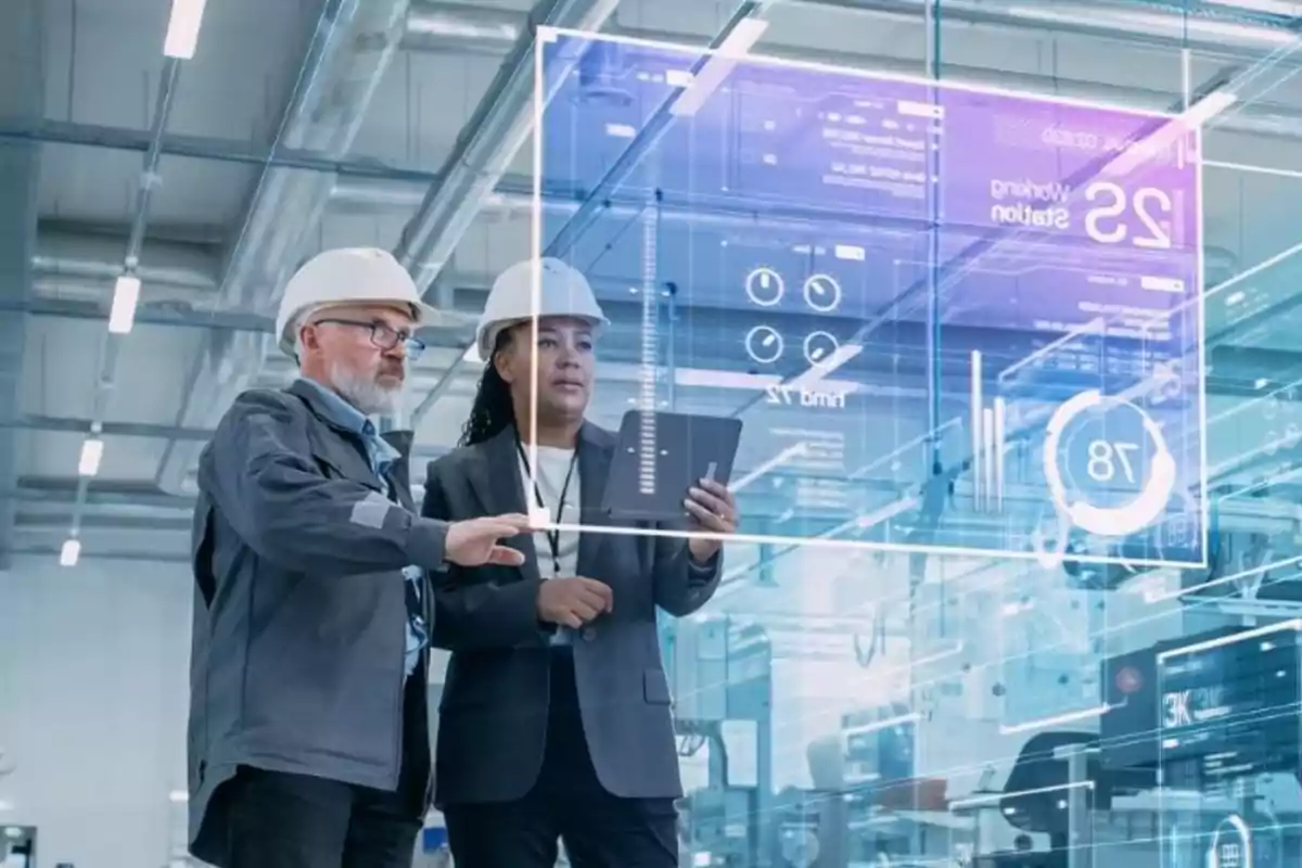 Dos ingenieros con cascos de seguridad revisan datos en una pantalla holográfica en una fábrica moderna.