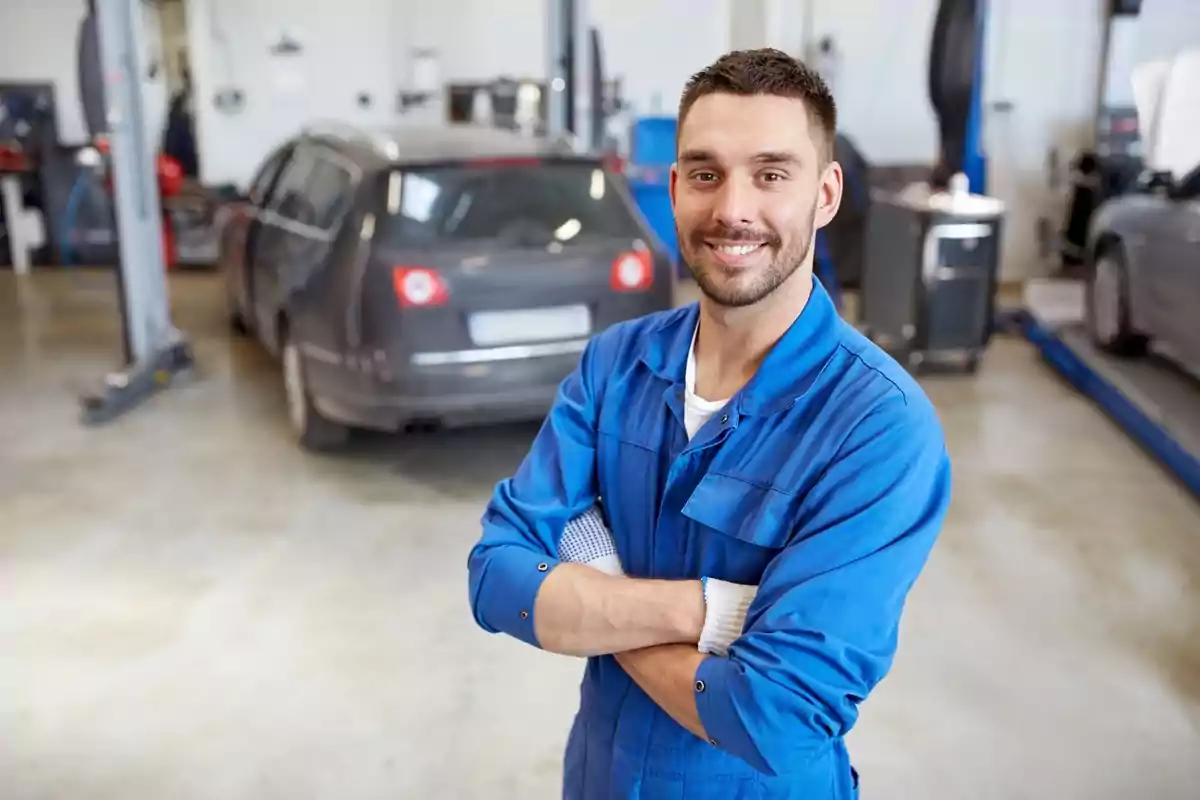 Mecánico sonriente con uniforme azul cruzando los brazos en un taller de automóviles.