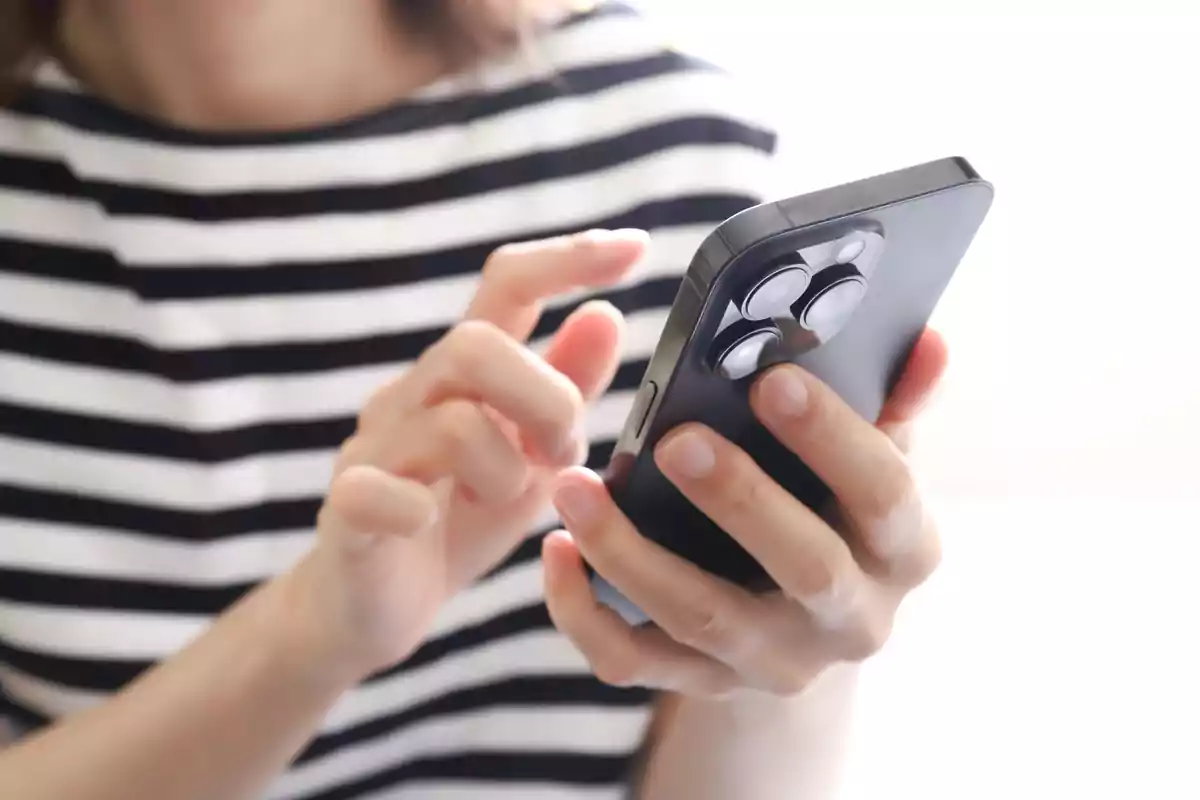 Persona usando un teléfono inteligente con una camiseta de rayas.