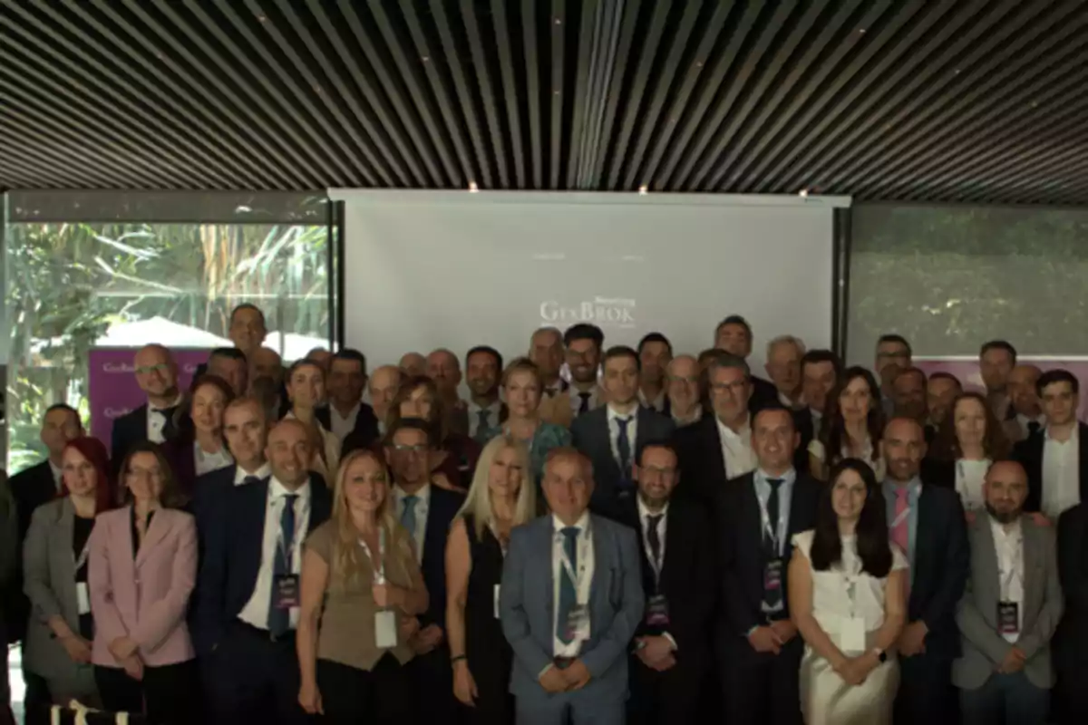 Grupo de personas vestidas de manera formal posando juntas en un evento corporativo en un salón con techo moderno y pantalla de proyección al fondo