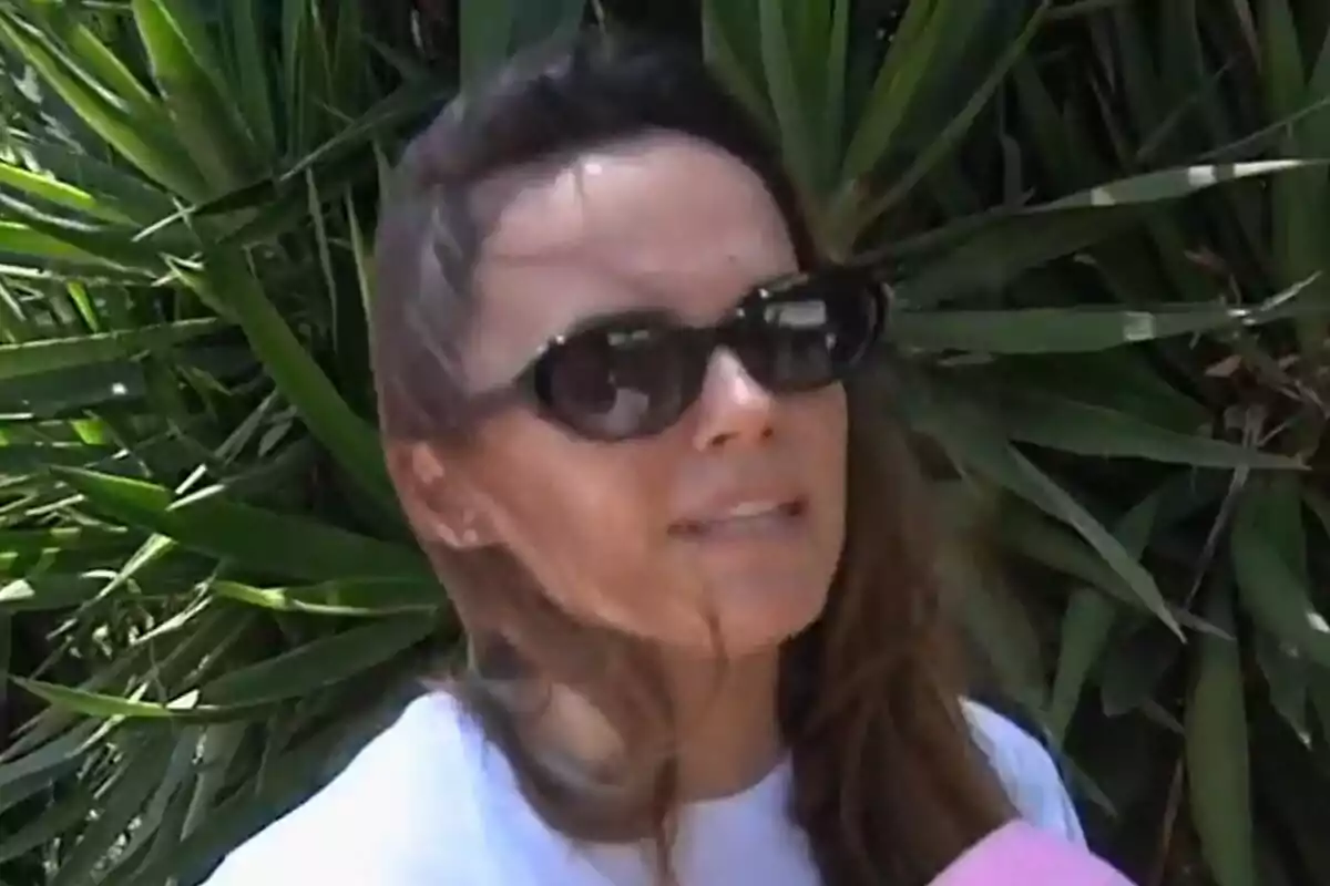 Melody con gafas de sol hablando frente a un micrófono rosa con plantas verdes de fondo en Vamos a ver. Melody con gafas de sol hablando frente a un micrófono rosa con plantas verdes de fondo en Vamos a ver.